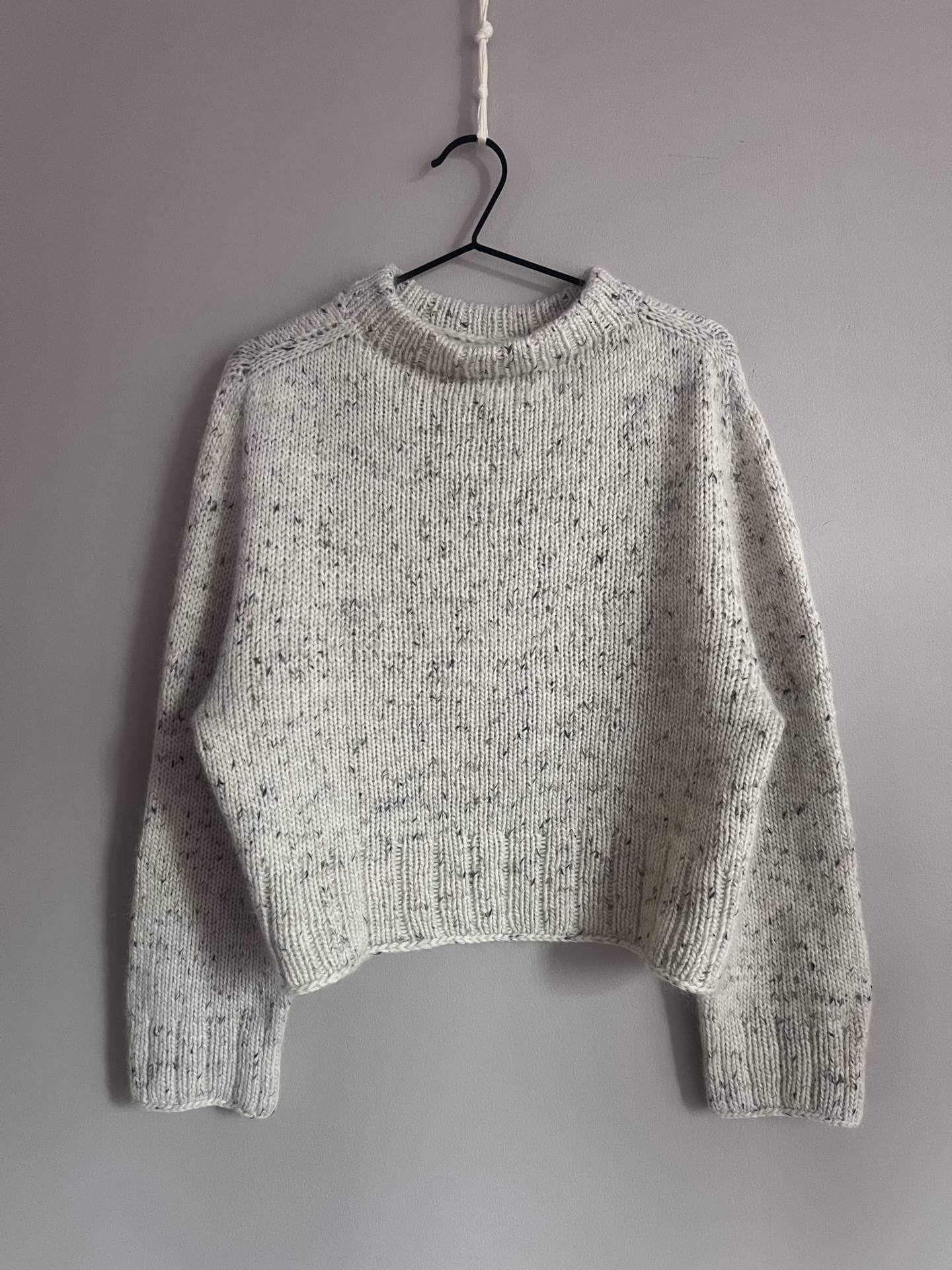 Hvit strikket genser foran hvit bakgrunn. Strikkepakke og strikkeoppskrift - Suits me fine genser er en klassisk strikket genser i merinoull og silk mohair.